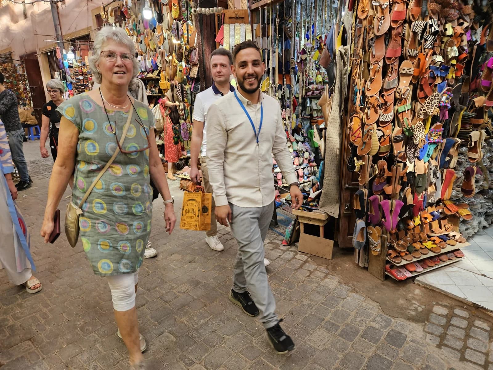 A guide and visitors walking past leather slippers in a Marrakech souk